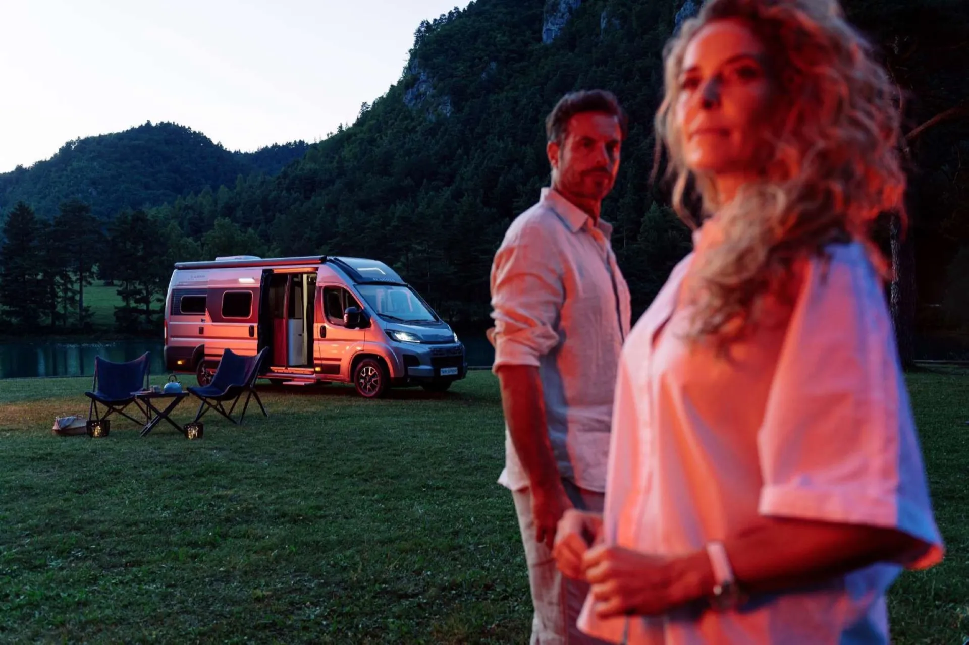 Couple au crépuscule devant leur fourgon Neo-NOMAD aménagé, au bord d'un lac de Provence